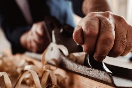 Hand führt einen Hobel über Holz.
